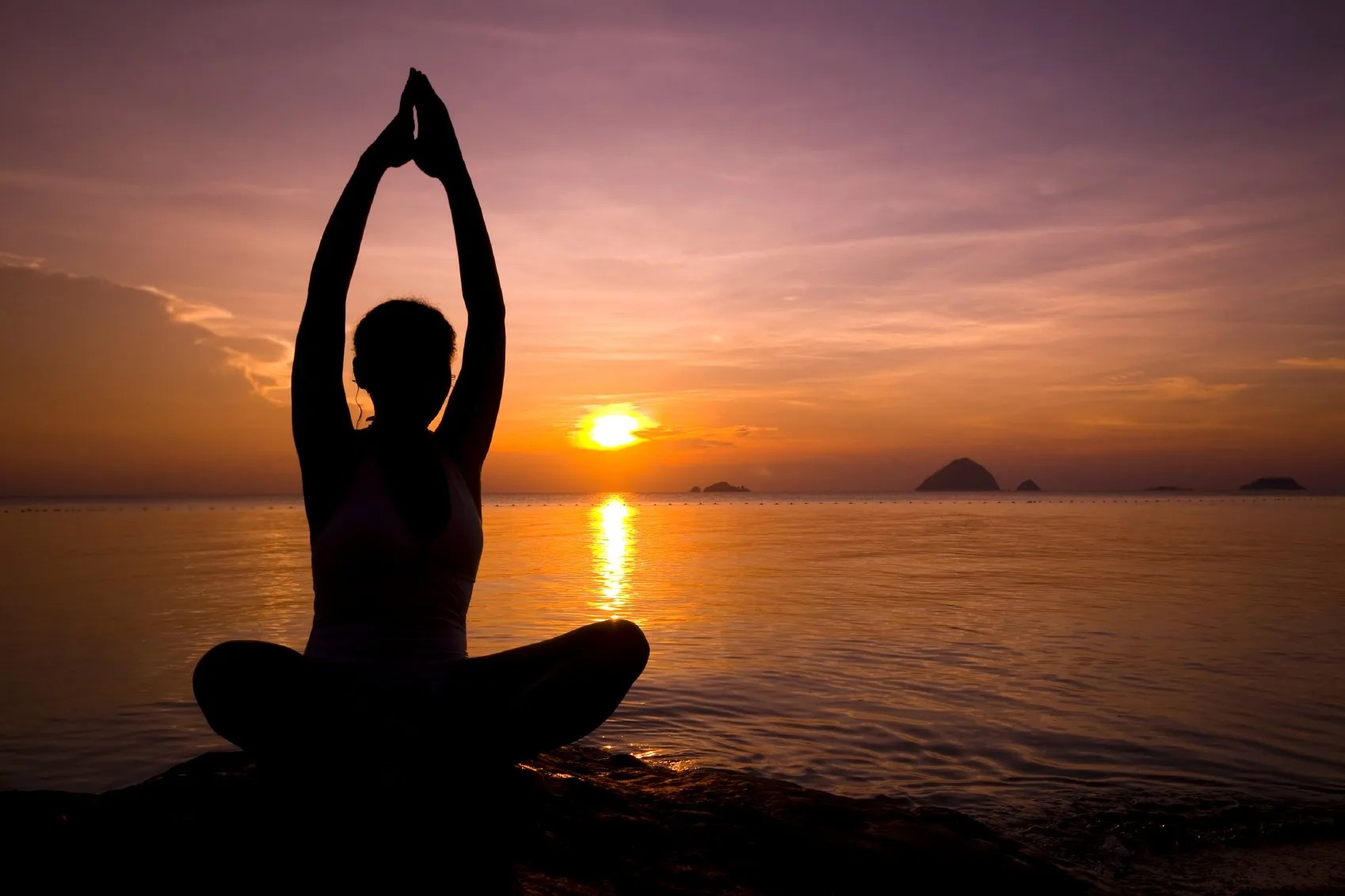 Woman practicing seated yoga and mindful movement by the ocean with traditional drums nearby.